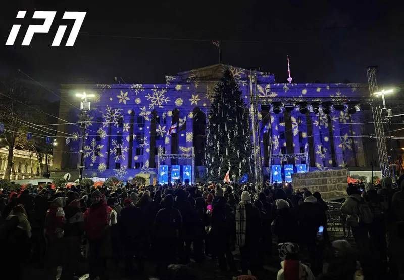 The front facade of the Parliament building is illuminated with New Year's decorations. Screens with the inscriptions "Tbilisi City Hall wishes you a Happy New Year" and "A city full of victories" are set up next to the Christmas tree
