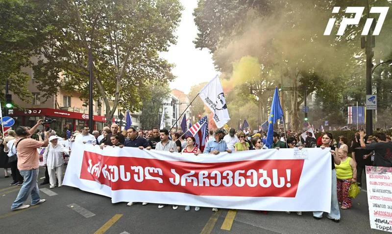 一场抗议游行正在从第比利斯州立大学的第一座大楼向议会进发，口号是“反对俄罗斯选举”。